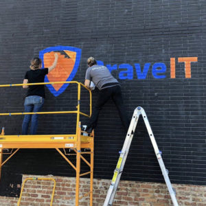 NPB Studio artists painting Brave IT logo on wall