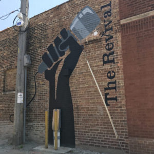 Outdoor mural on brick of hand holding microphone and text reading "The Revival"