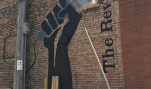 Outdoor mural on brick of hand holding microphone and text reading "The Revival"
