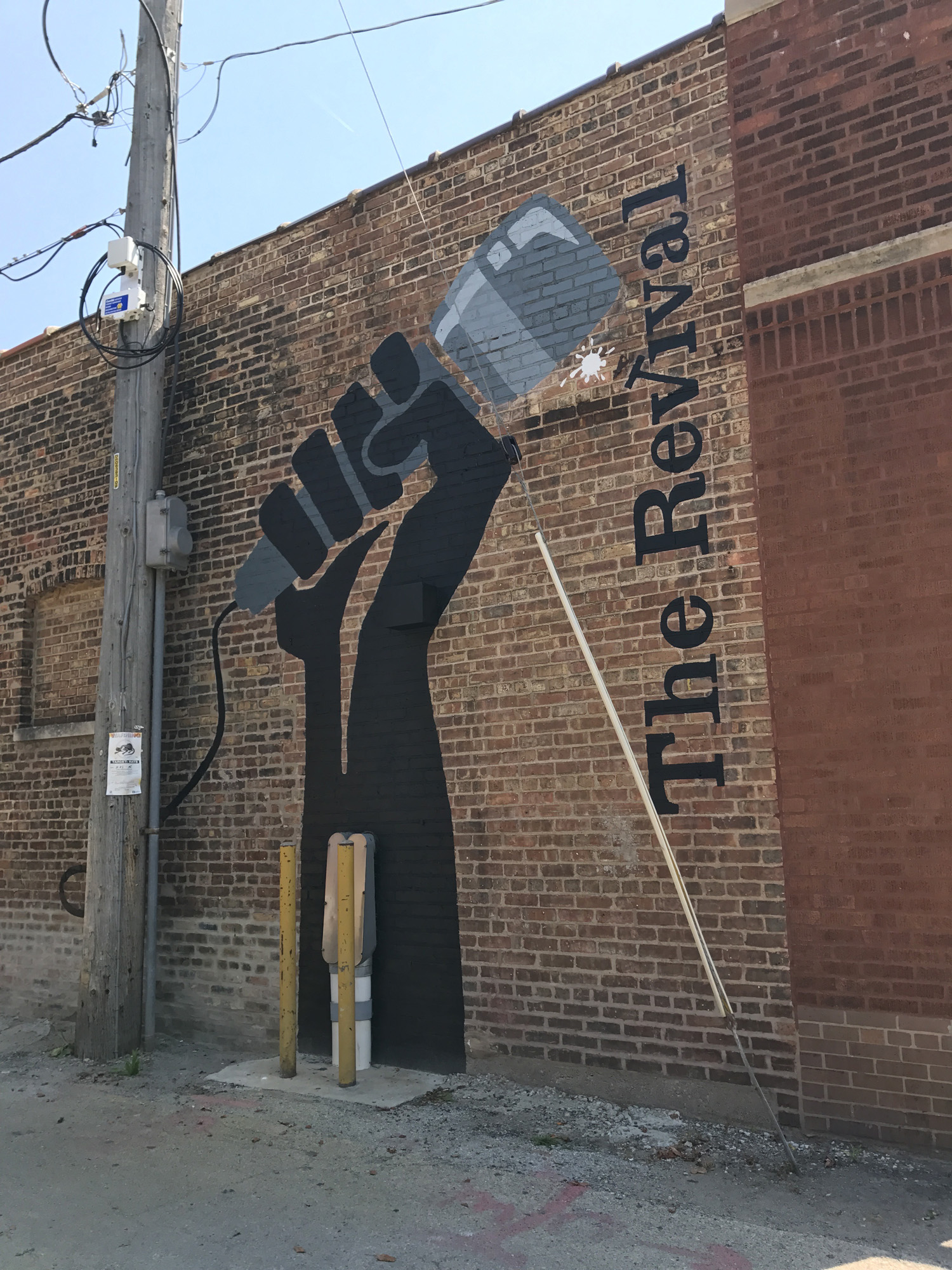 Outdoor mural on brick of hand holding microphone and text reading 