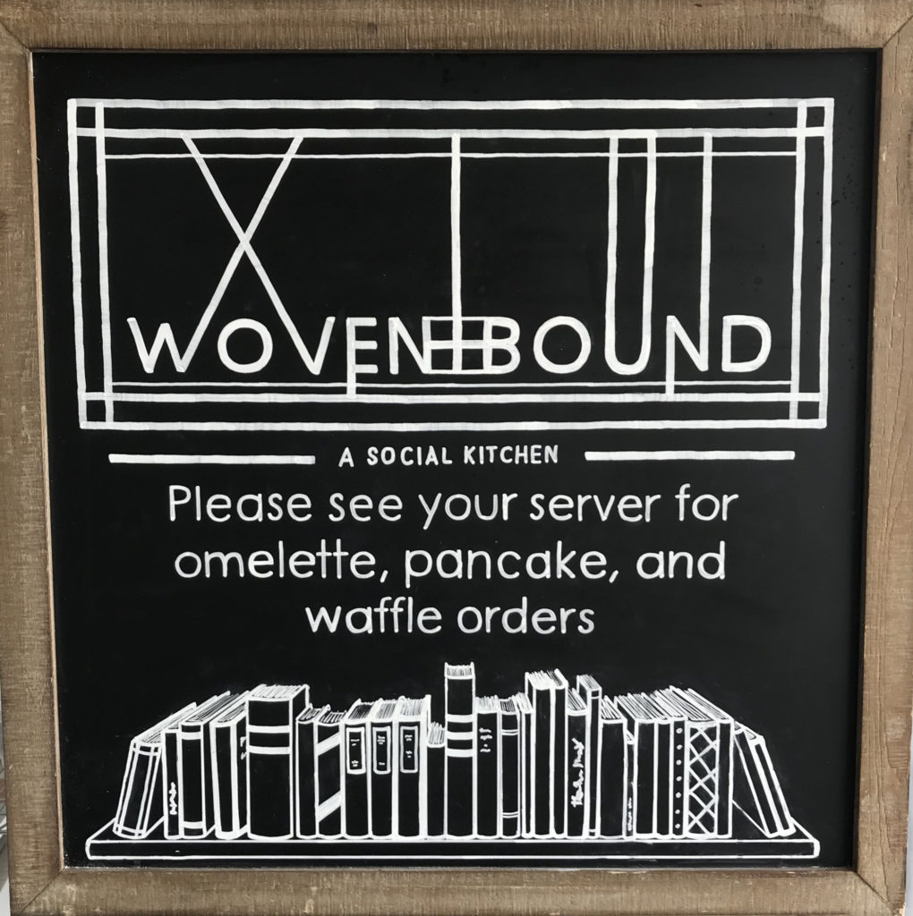 Chalkboard with text "Please see your server for omelette, pancake, and waffle orders" and image of shelf of books 