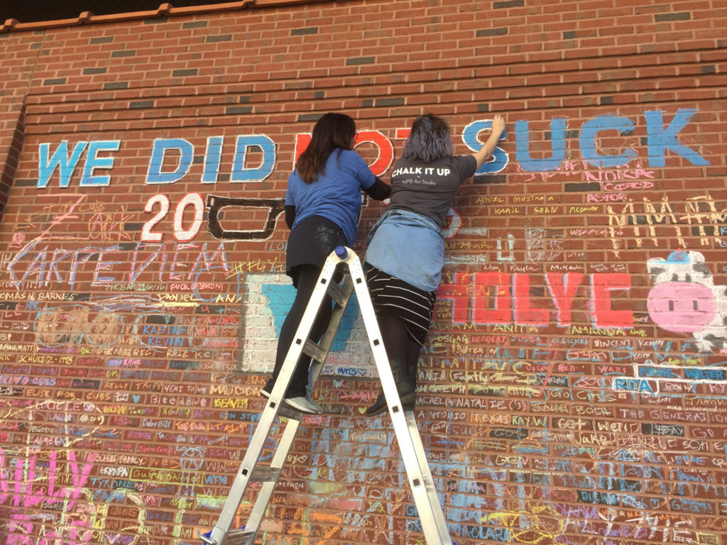 NPB studio artists standing on a ladder creating chalk art on the brick wall of Wrigley Field
